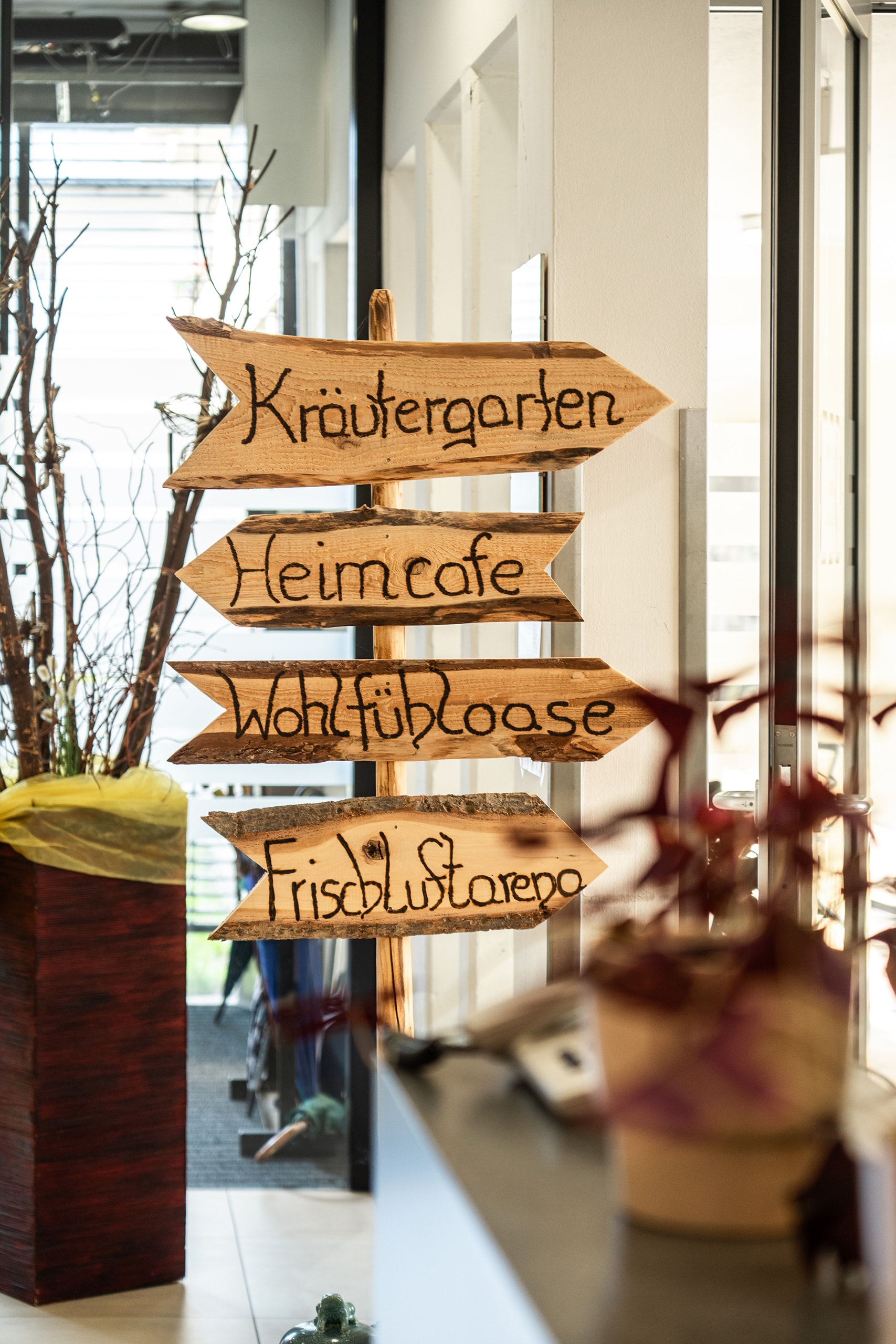 Holzwegweiser im Wohn- und Pflegeheim Lienz mit Hinweisen zu Kräutergarten, Heimcafé und Wohlfühloase.