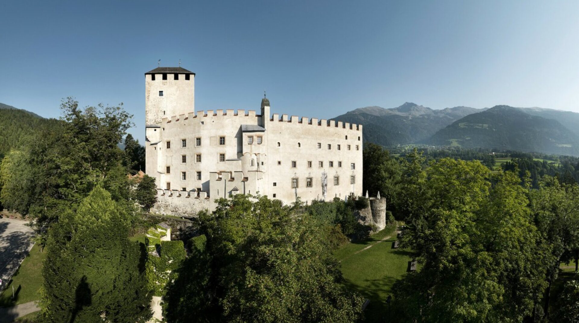 Historisches Schloss (Schloss Bruck) mit Wehrmauern und Turm in einer grünen Landschaft.
